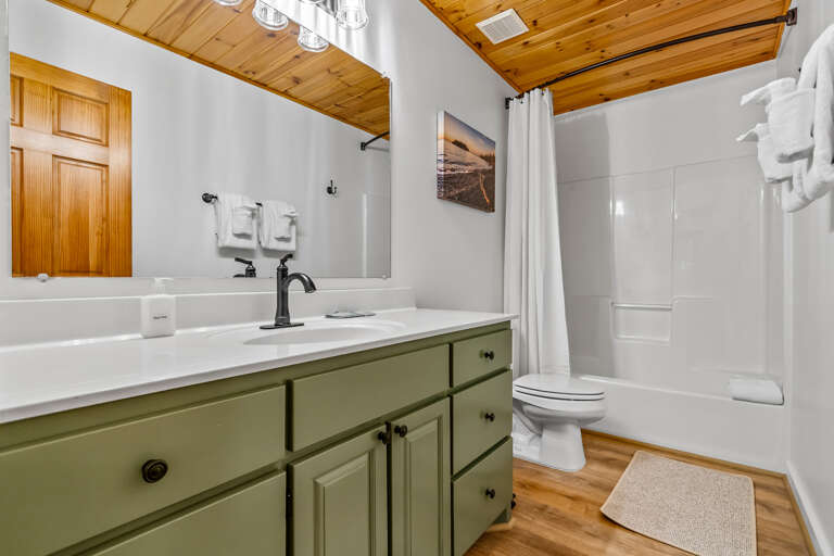 Step into your private bathroom with warm wood ceilings and fresh towels waiting for you. The crisp white tub-shower combo and soft lighting create a cozy, calming retreat after exploring.