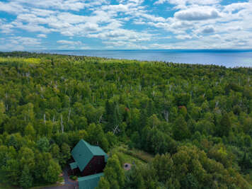 Aerial view of a secluded lakeside retreat surrounded by lush forest, offering peaceful natural surroundings and serene water views in the distance.