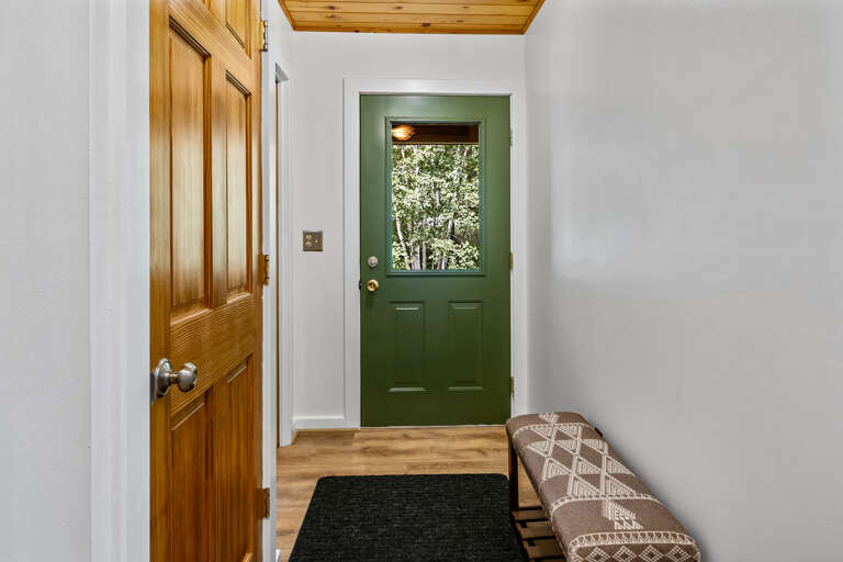The charming green entry door welcomes you inside, where warm wood accents and natural light create an inviting first impression. A cozy bench offers a convenient spot to slip off your shoes after a day of exploring.