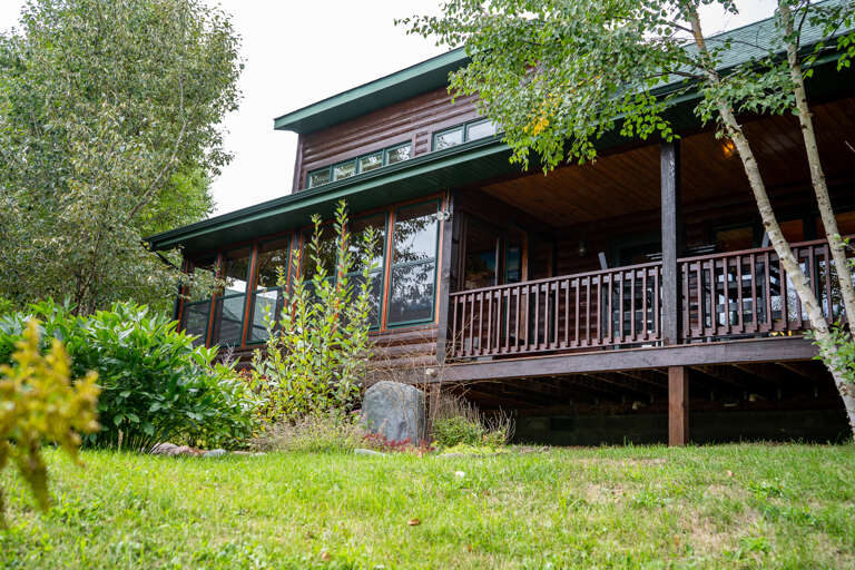 A modern mountain retreat nestled among tall pines and natural stone landscaping, offering a warm welcome to your woodland escape.