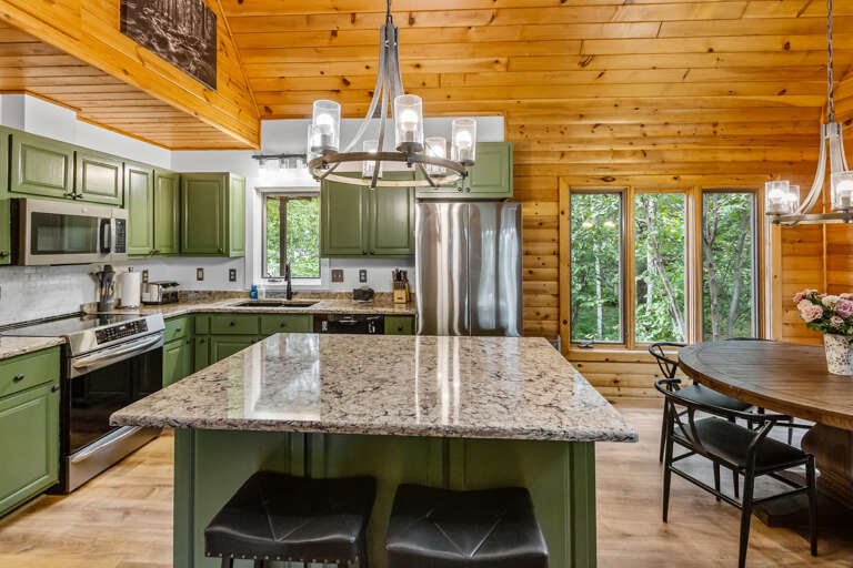 Your cozy cabin kitchen blends rustic warmth with modern ease, from olive-green cabinetry to granite counters and a bright island where you can gather over breakfast or evening meals.