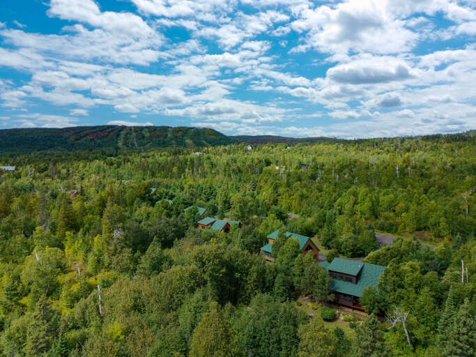 The property rests nestled among lush forests with mountain ridges visible in the distance, offering a peaceful woodland setting for a secluded retreat.