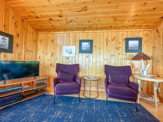 There is a TV and two comfy lounge chairs in the living room.