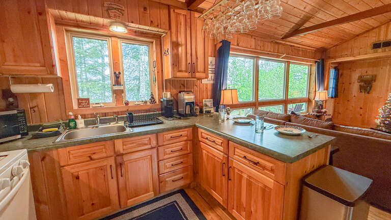 Cook your favorite meals in this fully equipped kitchen with warm wood tones and large windows framing views of the surrounding trees, making every moment here feel like a true cabin escape.