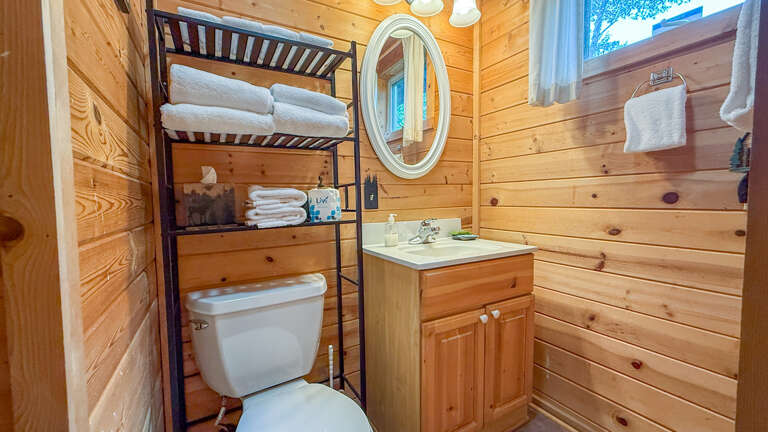 Your cozy cabin bathroom features warm wood paneling, a vanity with storage, and fluffy towels ready for you. Natural light streams in, making freshening up feel like part of the escape.