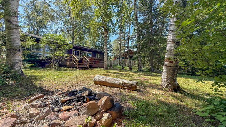 The property sits nestled among birch and pine trees, with a welcoming fire pit area perfect for cozy evening gatherings surrounded by nature.