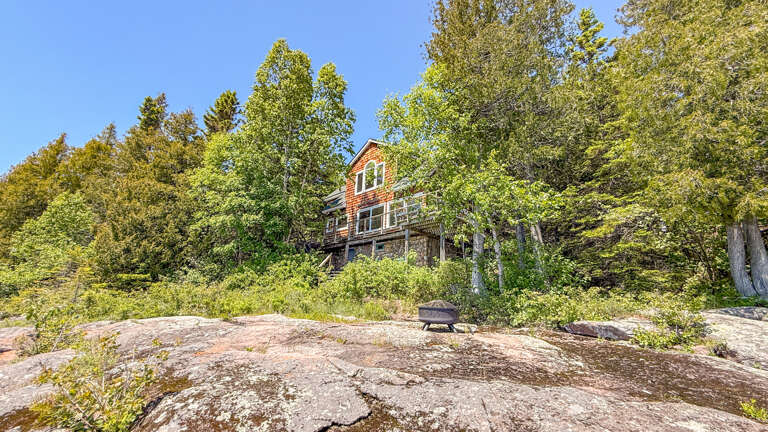 A secluded wooden cabin nestled among towering trees on a natural rock outcropping, offering a peaceful retreat surrounded by lush forest scenery.
