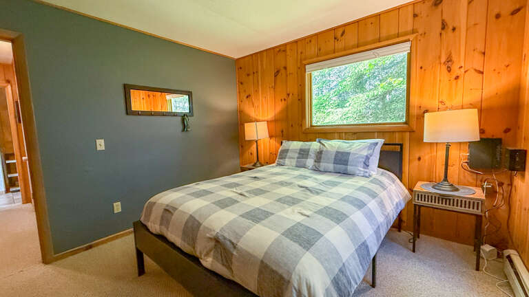 Unwind in this cozy bedroom with warm knotty pine accents and soothing colors. Your plush bed frames a window view of lush greenery, inviting natural light and fresh forest breezes into your retreat.