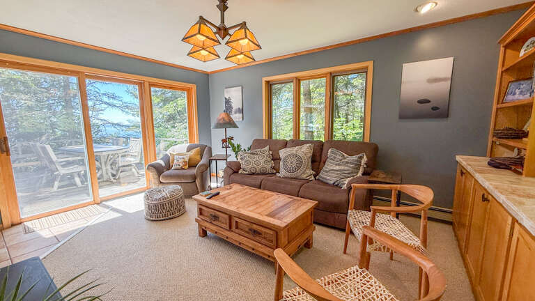 Unwind in your cozy living room where sunlight streams through floor-to-ceiling windows, inviting you to relax on plush seating while enjoying peaceful water views from your private deck.