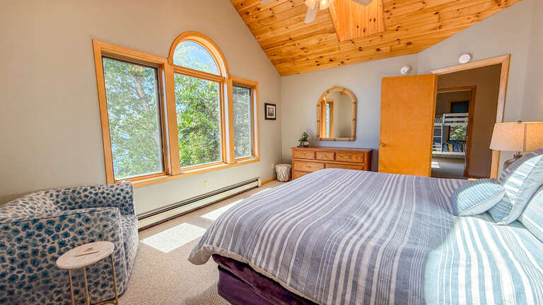 Wake up to sunlight streaming through tall arched windows and enjoy forest views from your cozy bedroom retreat. Warm wood accents and thoughtful furnishings create a welcoming sanctuary for restful nights.