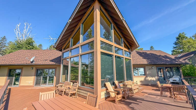 This stunning A-frame property nestled in a natural wooded setting offers an architectural showpiece of floor-to-ceiling windows and expansive outdoor decking, perfect for relaxing in fresh mountain air under clear blue skies.