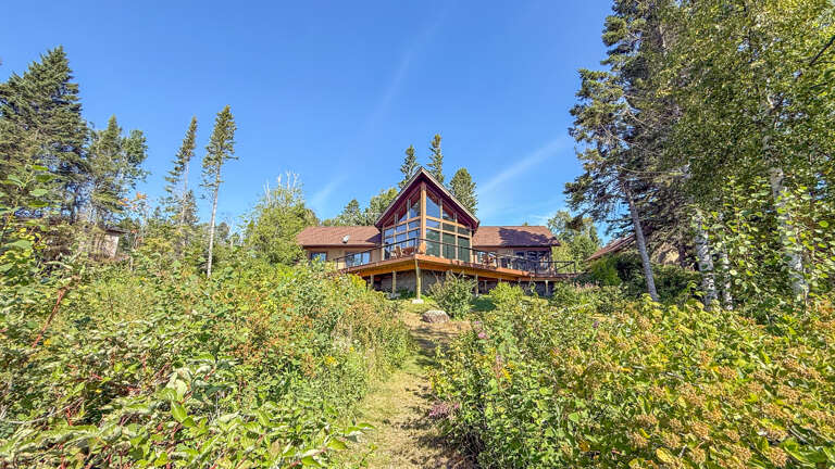 A beautiful cabin nestled in the forest, surrounded by towering evergreens and natural greenery. The property offers a peaceful retreat in nature with stunning mountain landscapes all around.