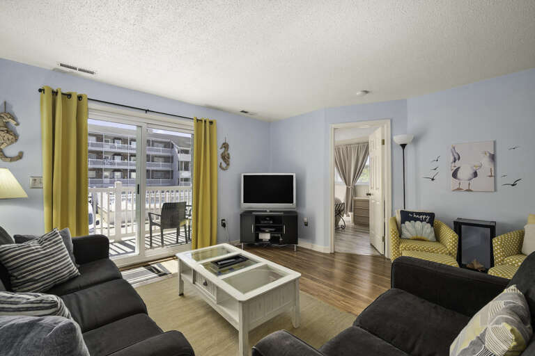 Bright Blue Living Room With Balcony Access, Black Sofas, Yellow Curtains, And Hardwood Floors