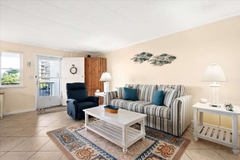 Light-filled Living Space In Vacation Rental With Striped Sofa, Blue Armchair, And Balcony Access