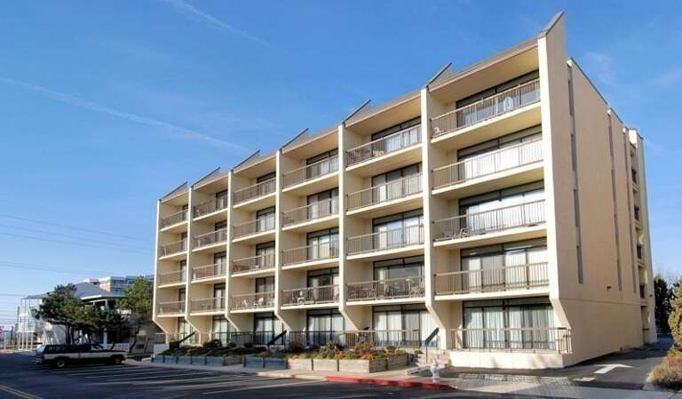 Beige Building Beneath Blue Sky, Balconies Bathed In Sunlight