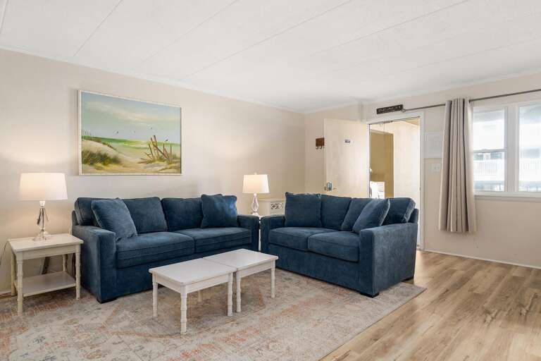 Bright Beachside Vacation Rental Living Space With Blue Sofas And Light Wood Flooring