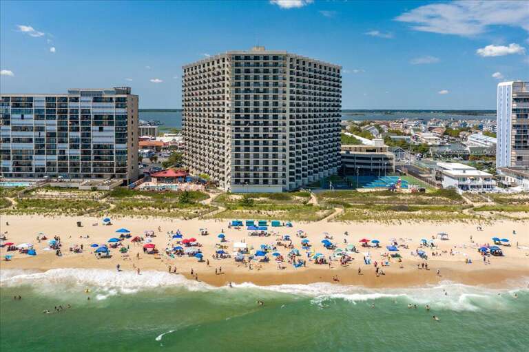 Aerial View Of Bustling Beach With Umbrellas, Waves, And High-rise Buildings