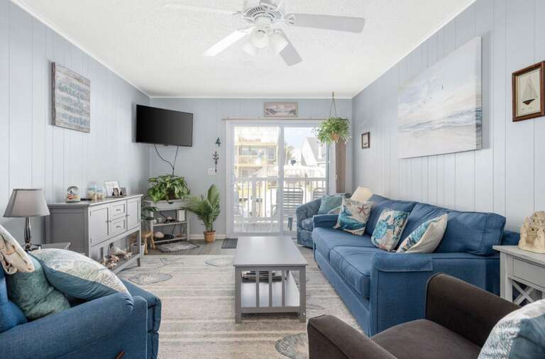 Light Living Room With Blue Sofas, Pale Walls, And Breezy Balcony View
