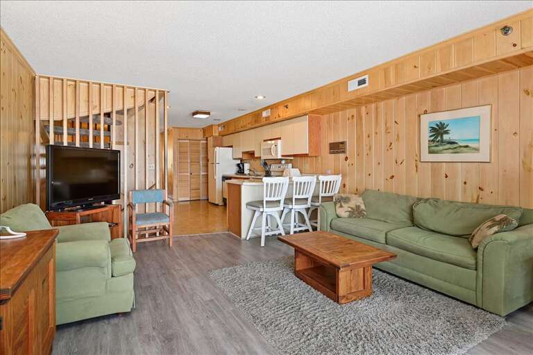 Spacious Living Space With Wooden Walls, Simple Seating, And Integrated Kitchen Area