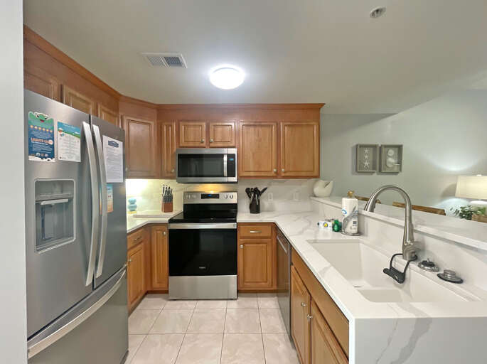 Brightly Lit Kitchen With Wooden Cabinets And White Countertops In A Vacation Rental