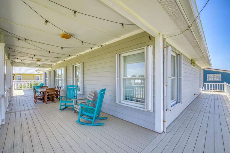 Seaside Structures Spacious Deck With Rocking Chairs And Dining Set Under A String Of Lights