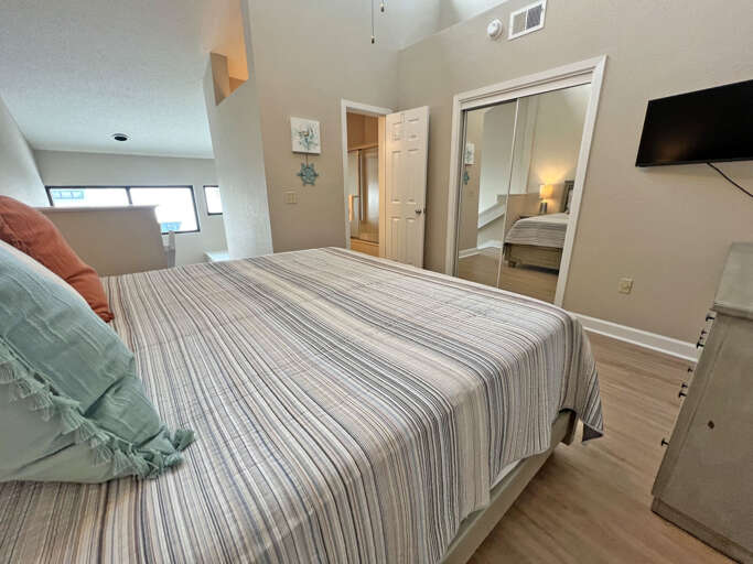 Bedroom With Striped Bedding, Mirrored Closet Door, And Wall-mounted TV