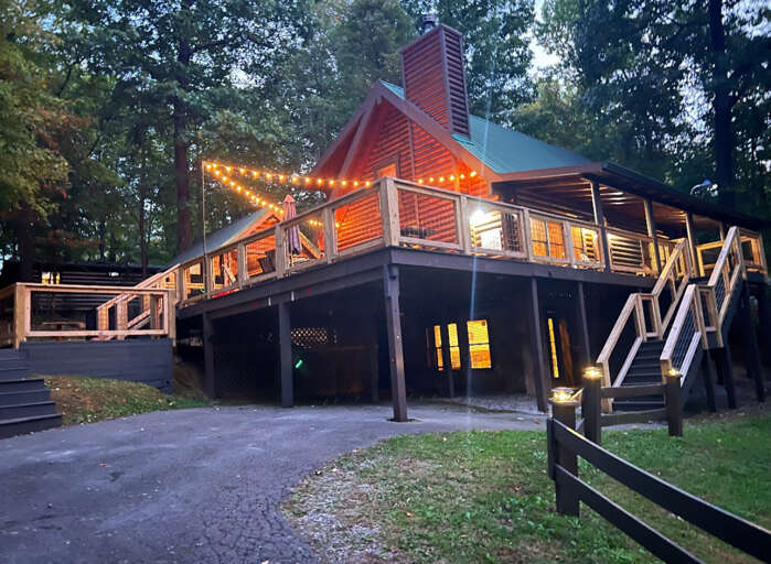 Wooden Cabin With Lit Lanterns And Lengthy Staircase Amid Lush Leaves