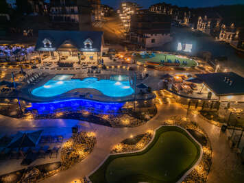 Nighttime Aerial View Of Lit Pools And Lounging Areas Surrounded By Buildings