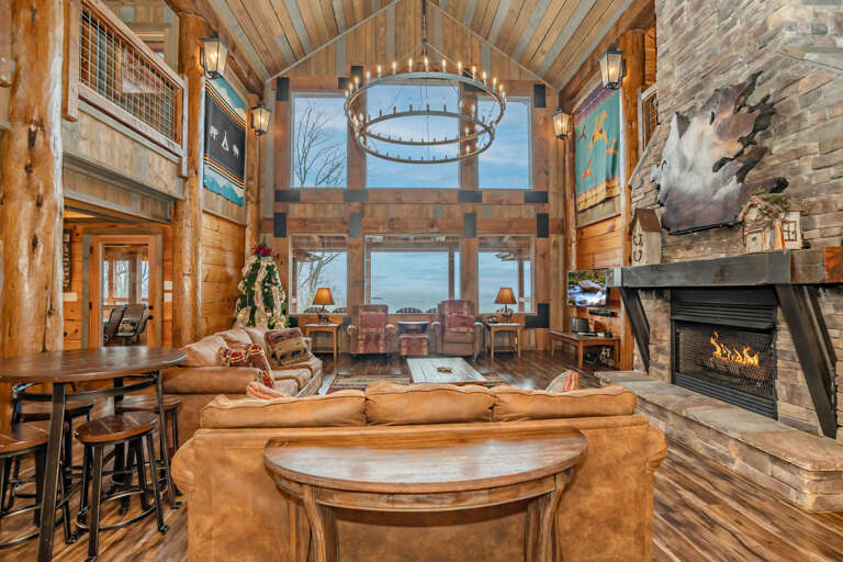 Rustic Room With High Ceilings, Panoramic Windows, And A Stone Fireplace