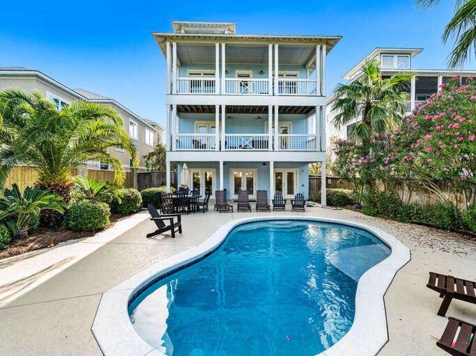 White Building With Balconies Behind Blue Pool, Flanked By Foliage