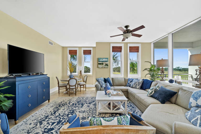 Bright Beachside Living Room With Blue And Beige Decor, Ceiling Fan, And Sliding Glass Doors Leading To Balcony