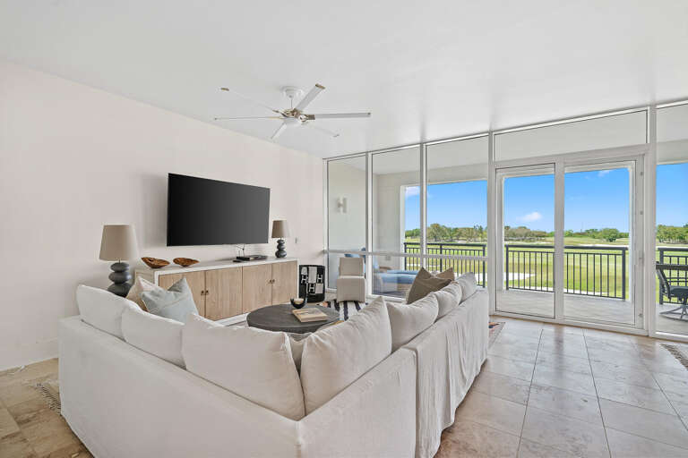Room With White Sofa, TV, Sliding Glass Doors Leading To Balcony Overlooking Green Landscape