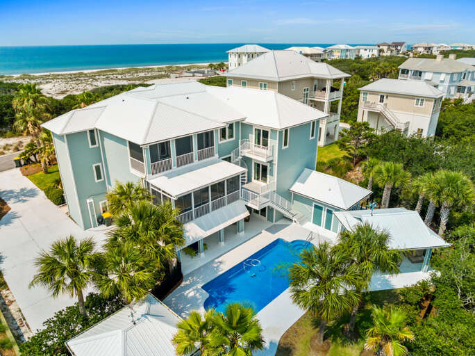 Aerial View Of Large Pale Blue House With Pool, Surrounded By Palm Trees, Near Beach