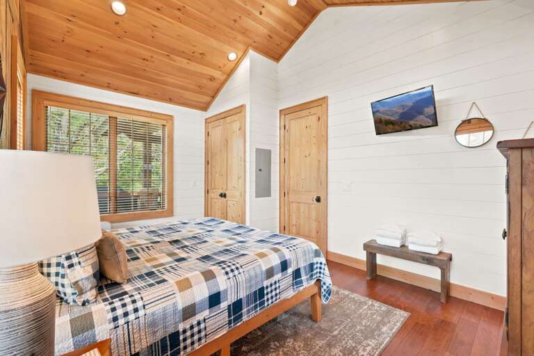 Sun-drenched mornings and cozy nights await in this warm wood bedroom at Banner Sky, with treetop views right outside the window.