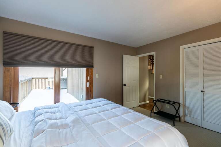 Simple Bedroom With White Bedding, Balcony Access, And Closed Closet Doors