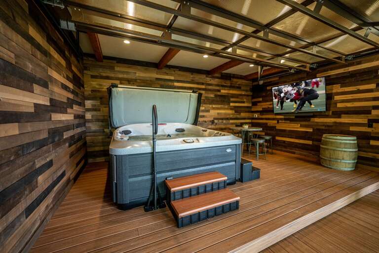 Lower level hot tub room with roll up garage door, seating area inside and out and large screen smart tv.