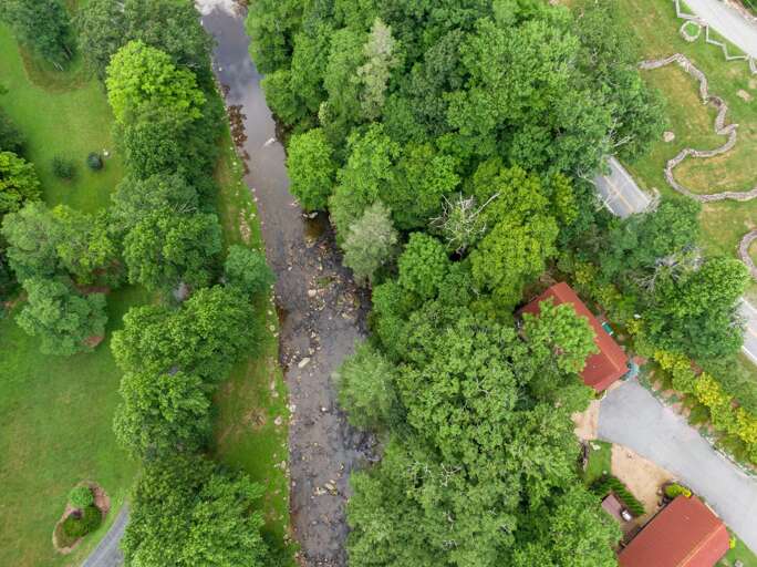Aerial View Of A Stream Flowing Through A Lush Green Landscape With Buildings Aerial View Of A Stream Flowing Through A Lush Green Landscape With Buildings