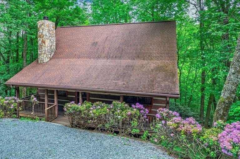 Rustic Retreat Nestled In Lush Greenery With A Towering Chimney And Vibrant Flowers