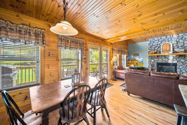 Rustic Room With Wooden Walls, Stone Fireplace, And Dining Table Near Deck Doors