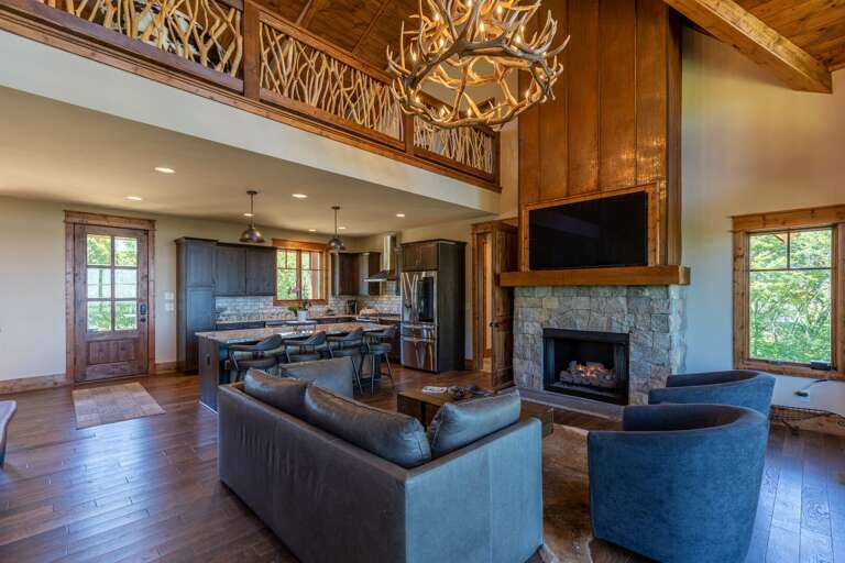 Spacious Living Area With Stone Fireplace And Wooden Accents, Adjoining Open Kitchen In Vacation Rental