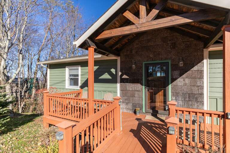 Wooden House With Sunny, Shadowed Porch And Bare Branches Behind