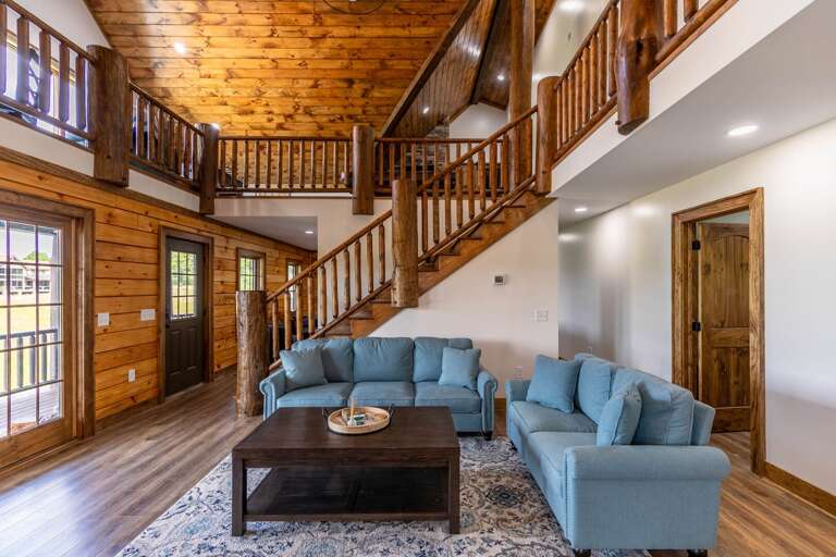 Spacious Lounge With Light Blue Sofas, Wooden Staircase Leading Upstairs In A Rustic Vacation Rental