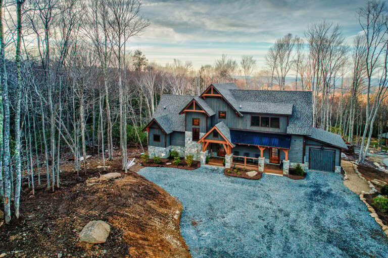 Large House Nestled Among Bare Trees With Vast Driveway And Blue-tinted Rooftops