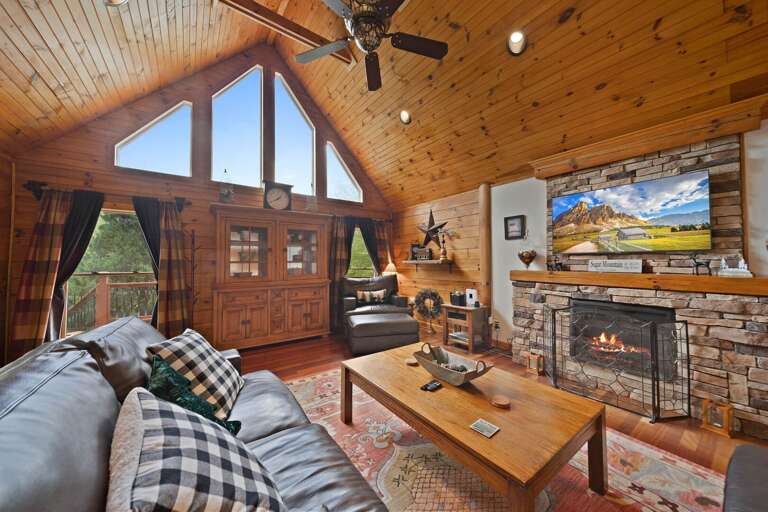 Wood-lined Living Space With Large Windows, Stone Fireplace, And Mounted Television