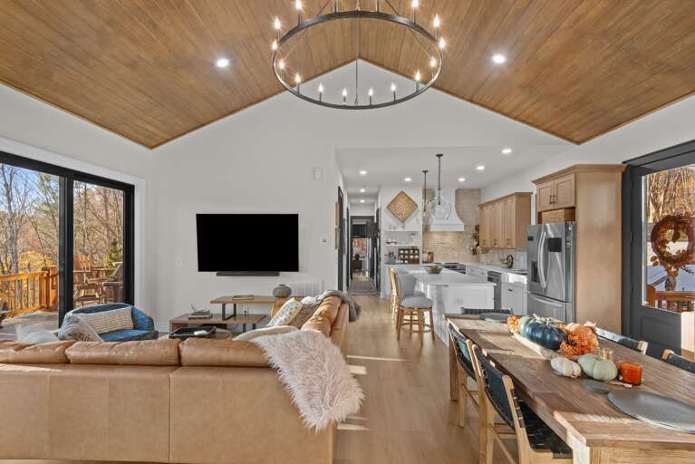 Spacious Living Space With Sleek Kitchen, Large Windows, And Wooden Ceiling