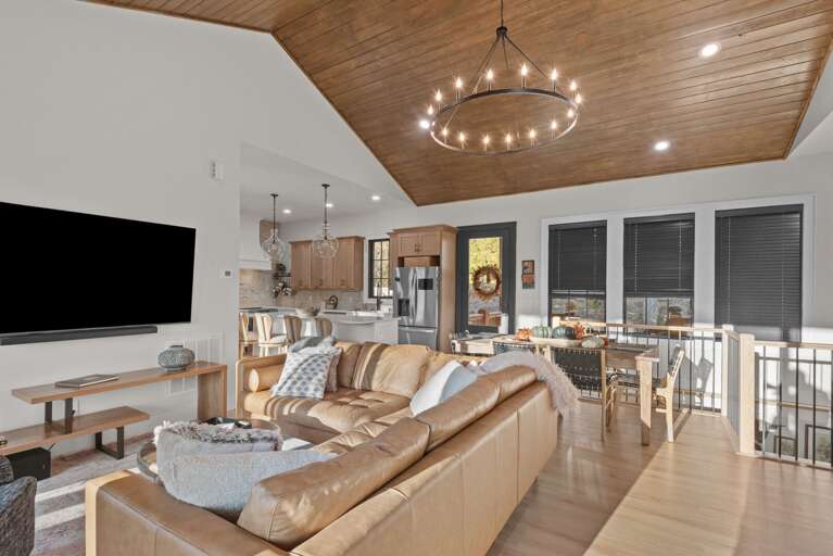 Spacious Living Area With Sleek Sofa, Stylish Circular Chandelier, And Integrated Kitchen