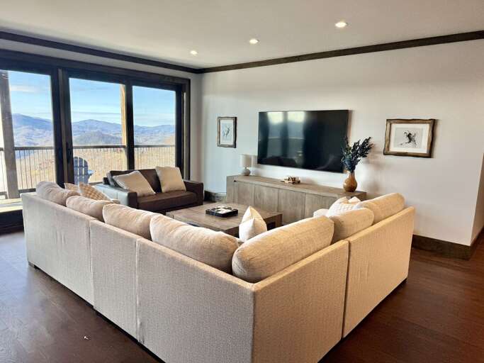 Living Space With Large Sofa Facing A Television, Surrounded By Scenic Mountain Views Through Expansive Windows
