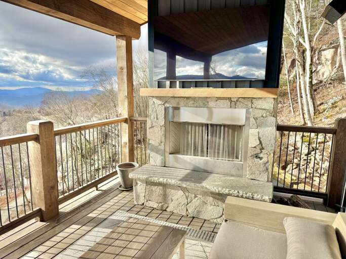 Balcony View Of Misty Mountains, Stone Fireplace, And Wooden Railings