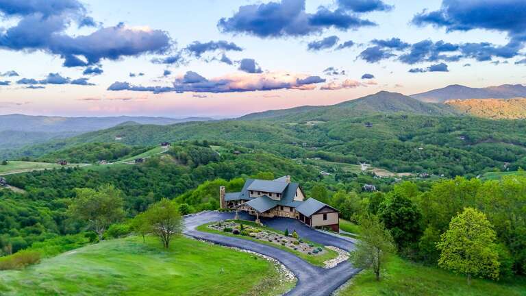 Aerial View Of A Large Building Nestled In Rolling Green Hills Under A Sunset Sky