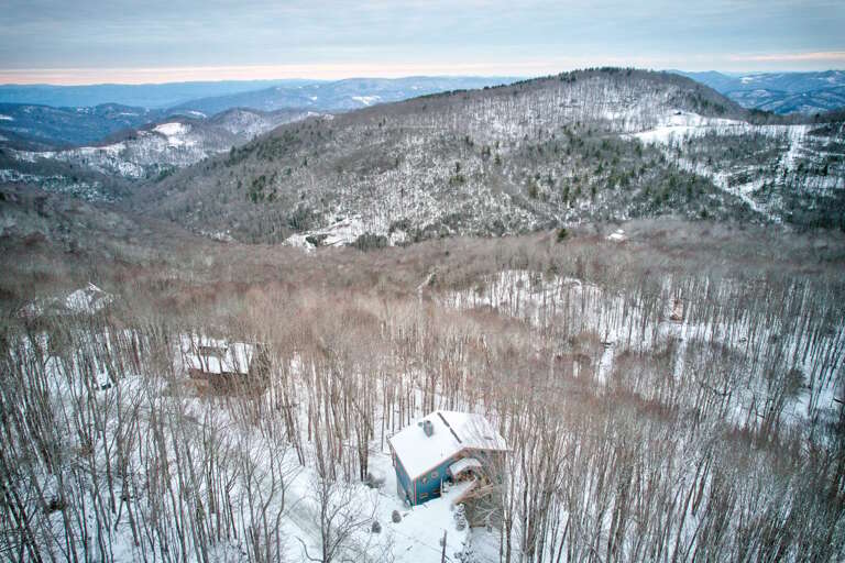 Snowy Scene Showing A Solitary Structure Surrounded By Skeletal Trees And Rolling Hills